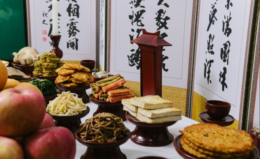 전통 제사상 위에 나물, 전, 두부, 산적, 과일 등이 가지런히 올려져 있고, 뒤편에는 한자로 된 병풍이 세워진 모습의 제사 차림 이미지.
